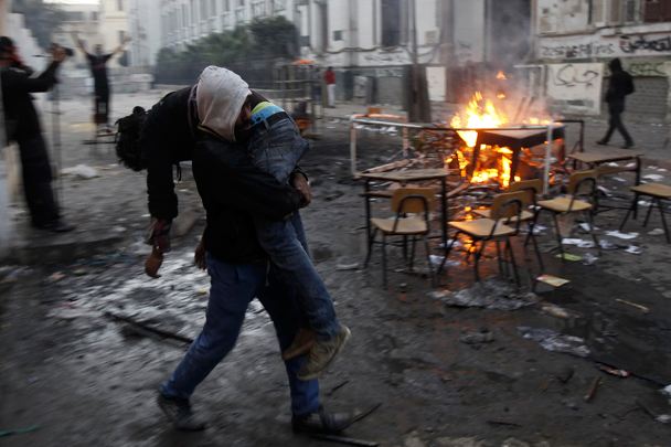 Участник оппозиционной манифестации несет на себе отравленного слезоточивым газом подростка. Другие манифестанты жгут мусор возле французской школы на улице Мохаммеда Махмуда, которая ведет к зданию МВД неподалеку от площади Тахрир в Каире в субботу