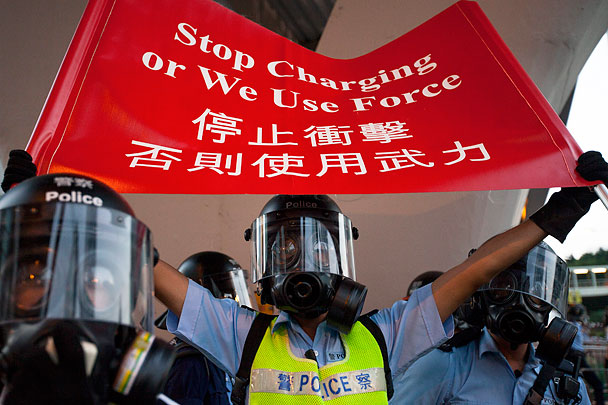 Полицейский держит плакат «Прекратите накалять обстановку, иначе мы применим силу» – официальное предупреждение властей Гонконга к протестующим