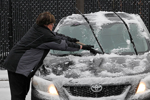 Женщина соскребает образовавшийся лед с лобового стекла своего автомобиля, припаркованного возле продуктового магазина в Миннеаполисе