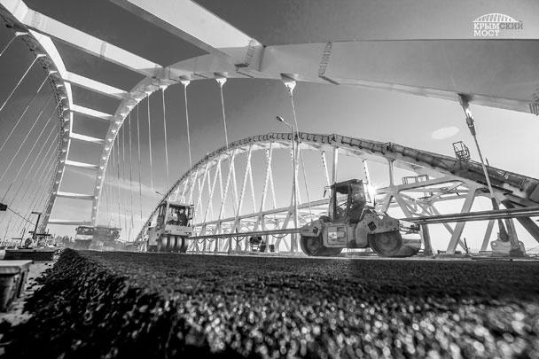 На автодорожной арке Крымского моста строители начали укладку асфальтобетона. На данный момент нижний слой уже готов, верхний уложат через несколько дней – после технологического перерыва. В целом дорожное покрытие пролета будет двухслойным с толщиной в 11 см